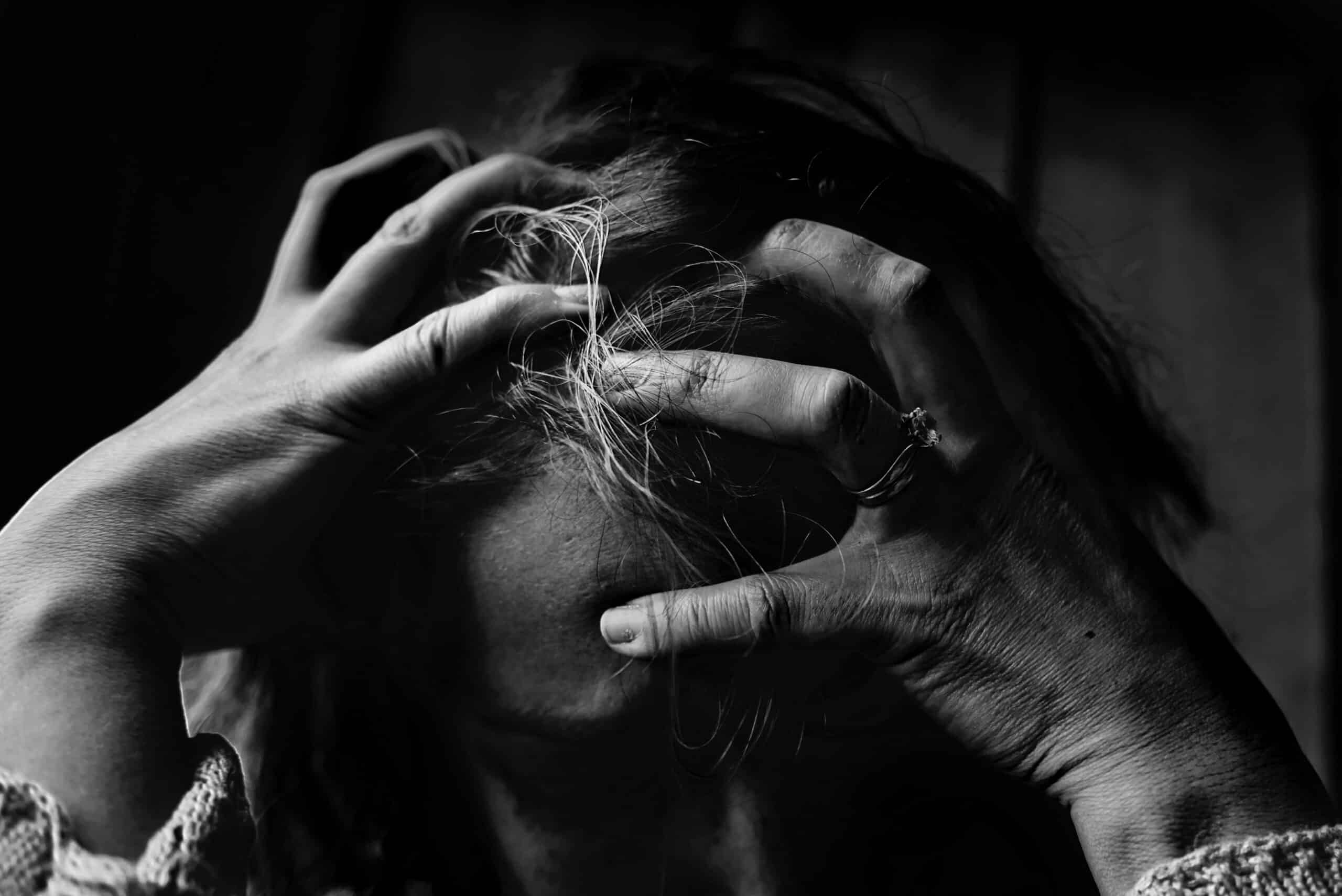 A black and white photograph of a woman sitting with her head in her hands, appearing stressed and overwhelmed