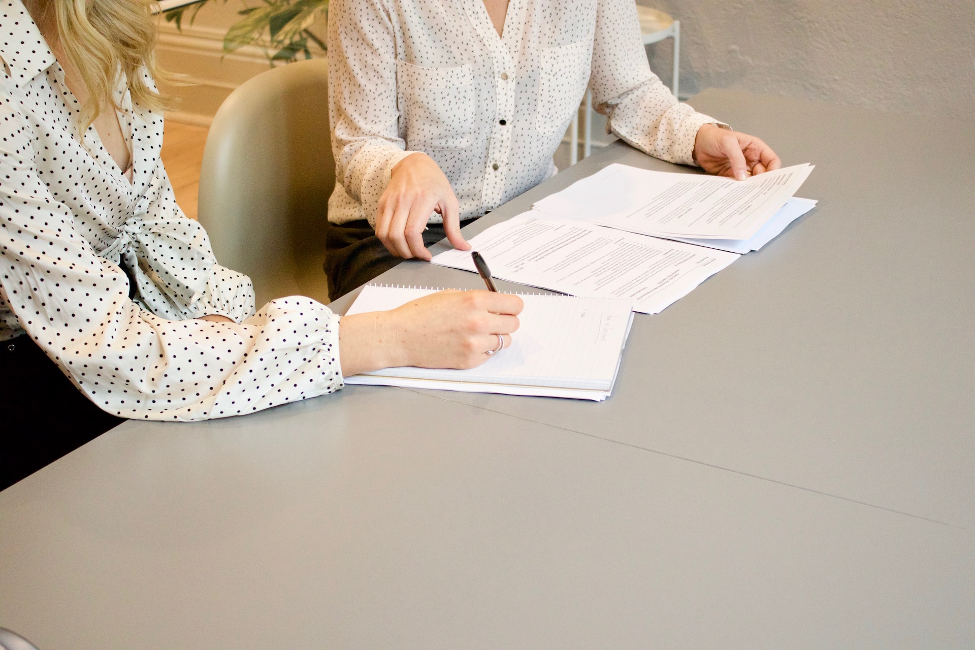 Two women with their hands on the table holding papers. 