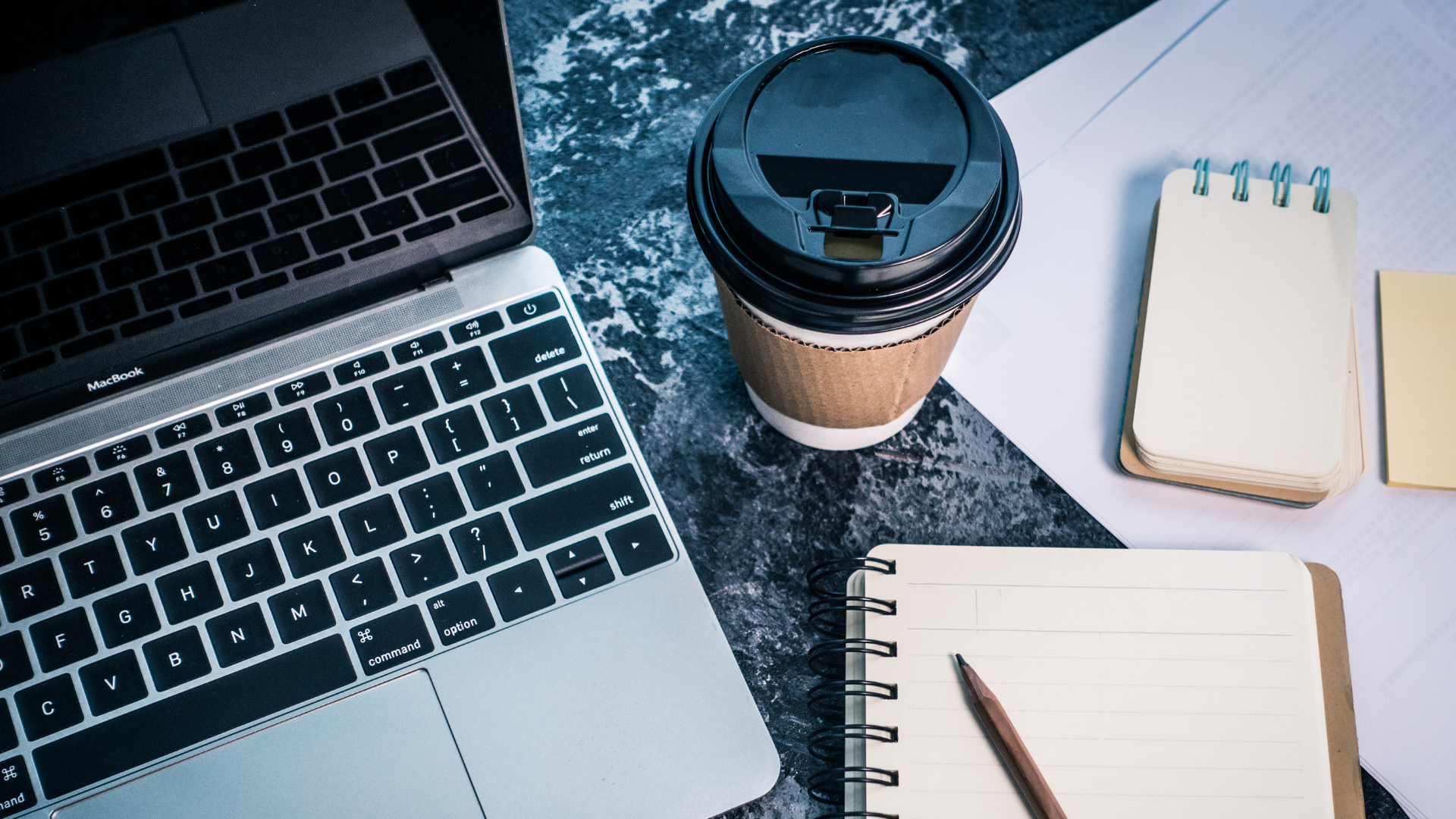 a laptop, a coffee and some notes on a desk
