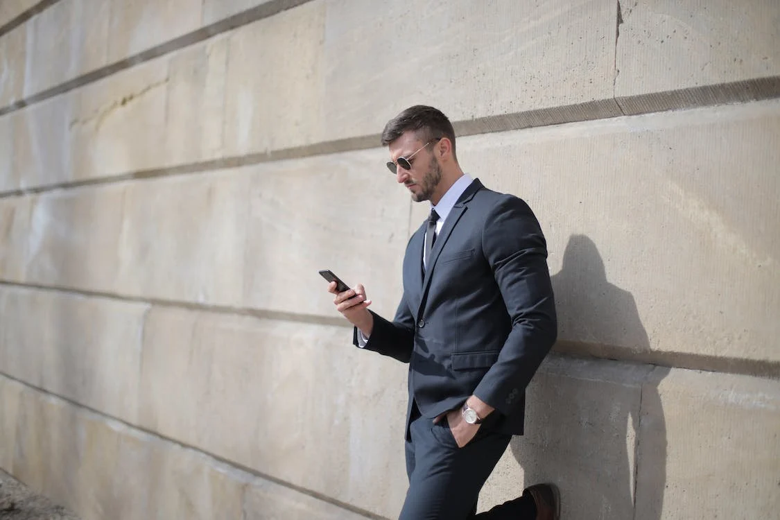 a man in a grey suit looking at his mobile phone and posing near the wall what to wear to a job fair